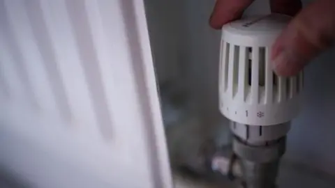 PA Media Hand adjusting a thermostat on a radiator.