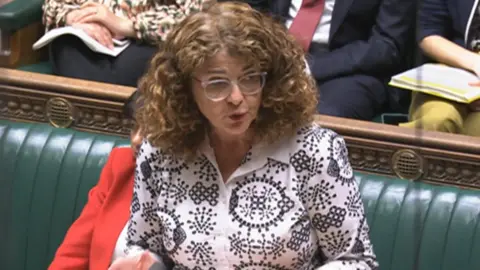UK Parliament The minister, wearing a black and white blouse, stands at the government front bench in the Commons