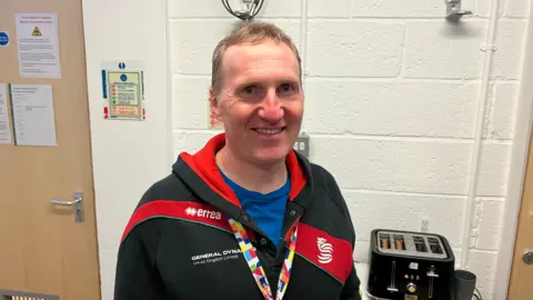 BBC/ RICHARD EDWARDS Matt Fisher, a community worker at the charity Up for Yorkshire, is looking straight into the camera. He is wearing a multi-coloured lanyard and a red-and-black tracksuit top