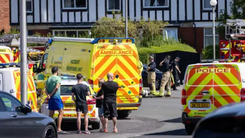 PA Media Locals look on as ambulance and police block the street