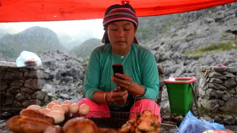 AFP An ethnic Hmong woman checks her phone at her market stall (Oct 2018)