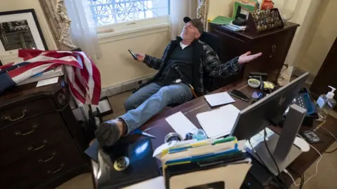 EPA A supporter of US President Donald Trump sits at the desk of US House Speaker Nancy Pelosi