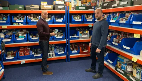 Max Wilkinson Two men surrounded by groceries at a food pantry