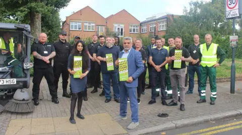 Brent Council Council leader Muhammed Butt stands with a council team, all holding green anti-fly-tipping posters