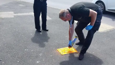 North Northamptonshire Council/ Google Maps A man standing on the road wearing blue gloves and spray painting an orange mark on to the road.