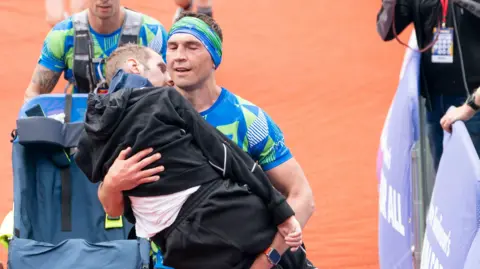 PA Media Sinfield carrying Burrow in an embrace as he crosses the finish line after a marathon