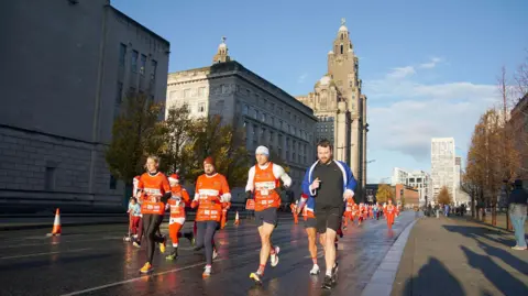 PA Media Kevin Sinfield running with three support runners with a sunlit Liver Building in the background
