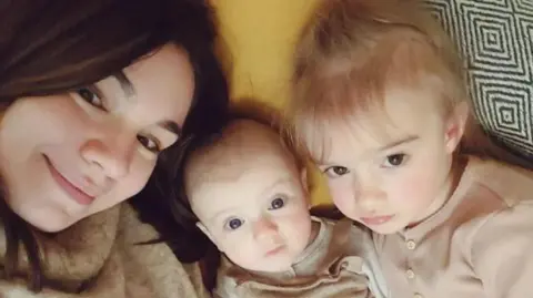 Judy Morgan A mum smiles at the camera with her two young children