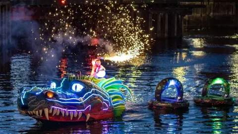 Drake Photography A man is waving a flare while riding the Monty the Mersey Monster display on a dock