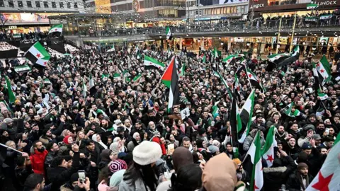 Reuters Very large crowd of people waving Syrian flags in Sergel's Square in Stockholm, Sweden December 8, 2024
Raised buildings and walkway barely visible in the distance