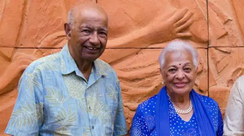 Flickr/East-West Center Gulab Watumull seen wearing a blue, patterned Aloha shirt with his wife Indru who is wearing a blue kurta with a pattern of white dots and a pearl necklace, in 2012
