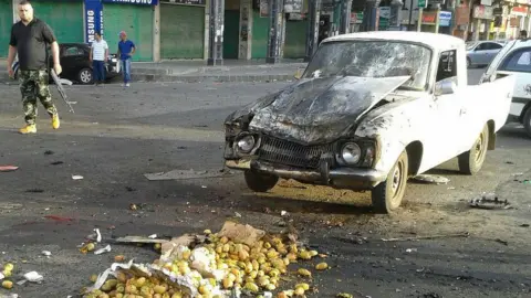 AFP Picture from Syrian news agency (Sana) on July 25, 2018 shows a member of the security forces walking past a truck damaged in a suicide attack in Suweida