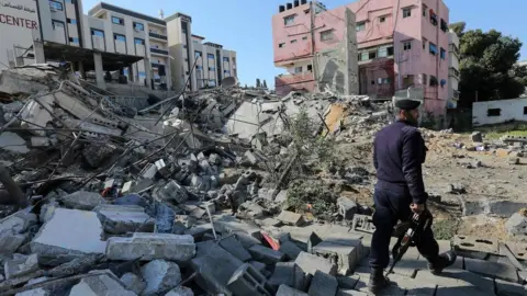 AFP Hamas policeman walks past the remains of a building in Gaza City destroyed in an Israeli air strike (26 March 2019)