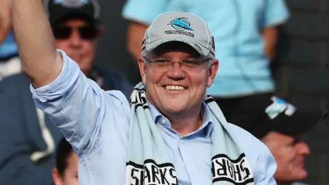 Getty Images Scott Morrison wearing a baseball cap and rugby scarf waves to the crowd while celebrating his victory at a rugby league match in Sydney on Sunday