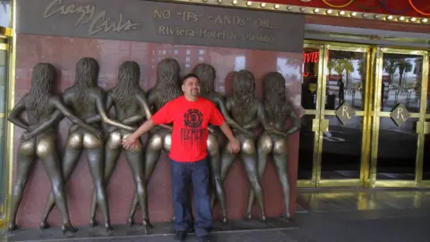 Getty Images A man poses with bronze statues showing Crazy Girls