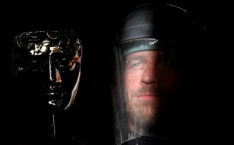 Toby Melville / Reuters Ray Terry, a furnace man at the foundry where the castings of the iconic British Academy of Film and Television Awards (BAFTA) masks are made, poses with a finished mask, ahead of the annual awards ceremony, London.