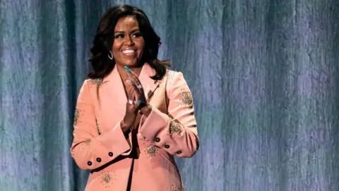 AFP Former US first lady Michelle Obama gestures on stage of the Royal Arena in Copenhagen on April 9, 2019 during a tour to promote her memoir "Becoming"