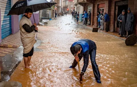 Getty Images A young man tries to unblock a gutter on a flooded street during stormy weather in Fnideq, Morocco - Friday 5 March 2021
