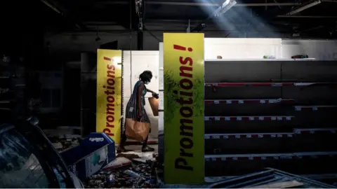 Getty Images A woman collects packets of groceries from a burnt down and looted Auchan supermarket in the up-market area of Almadies in Dakar, Senegal - Saturday 6 March 2021