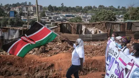 Getty Images A women waves the Kenya national flag as women human rights defenders from 26 community based organisations march to commemorate International Women's Day in Kibera, Nairobi, Kenya - Monday 8 March 2021