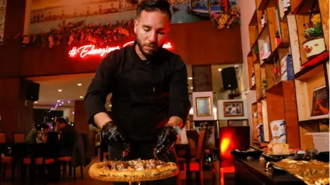Reuters Ahmed Hergal, founder of Italian restaurant L'antica Pizzeria DaPietro, adds ingredients to his pizza, covered with luxury foods and edible gold leaf, in Tunis, Tunisia - Saturday 6 March 2021