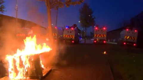 Alamy Police Land Rovers parked near a burning bin in Belfast