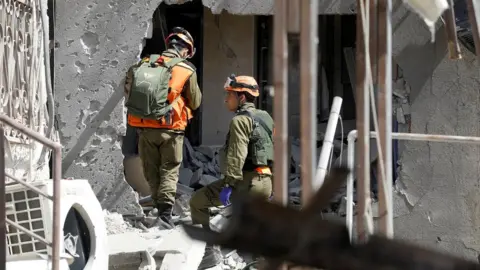 Reuters Soldiers work at a building damaged by a rocket launched from the Gaza Strip, in Ashkelon, southern Israel, May 11, 2021. REUTERS/Nir Elias