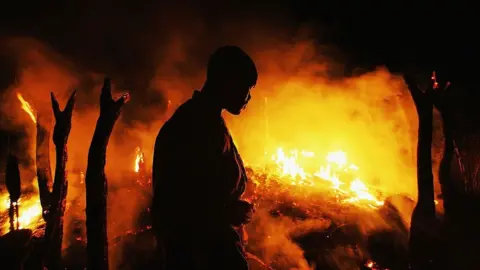 Getty Images A Sudanese rebel fighter from the Justice and Equality Movement (JEM) sombrely watches the abandoned village of Chero Kasi burn less than an hour after Janjaweed militiamen set it ablaze in the violence plagued Darfur region September 7, 2004.