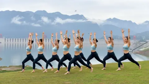 Getty Images People practice yoga at a park in front of the Three Gorges Dam to welcome the International Day of Yoga, in Zigui County on June 20, 2021 in Yichang, Hubei Province of China.