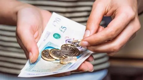 Getty Images A woman counts money in her hands