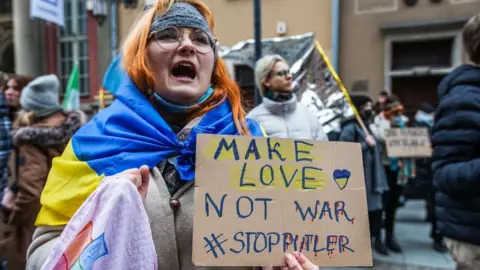 Getty Images Women draped with Ukrainian flag holds 'Make love not war' poster.