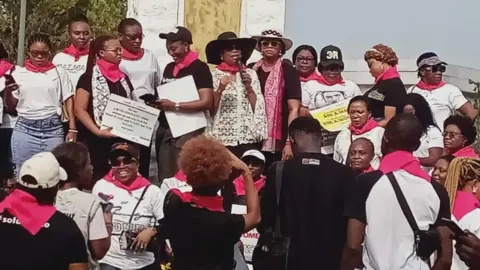 Grace Bassey Women wearing pink scarves protest outside Nigerian government building.