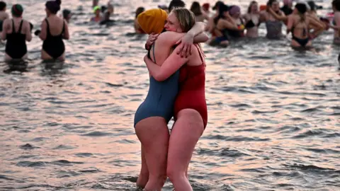 Getty Images Women embrace in sea wearing bathing suits.
