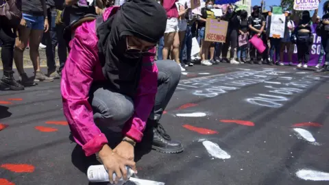 Getty Images Women wearing balaclava and spray paint bottle, sprays message on the ground.