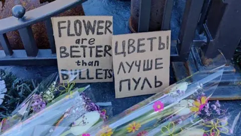Feminist Anti-War Resistance Flowers on WW2 memorial in Russia with a sign in Russian and English that reads, 'flowers are better than bullets'