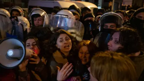 Getty Images Women surrounded by with police officers wearing helmets