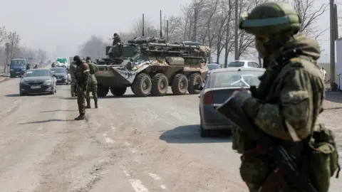 Reuters Service members of pro-Russian troops stand guard at a checkpoint in the course of Ukraine-Russia conflict in the besieged southern port city of Mariupol, Ukraine March 24