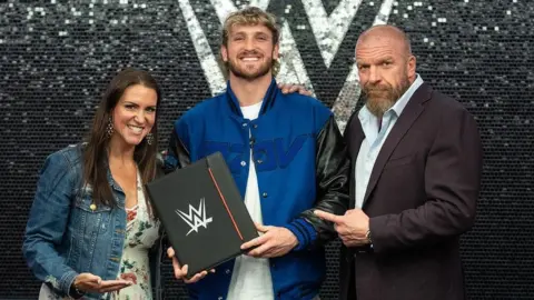 @LoganPaul Logan Paul stands with Stephanie McMahon and her husband Triple H