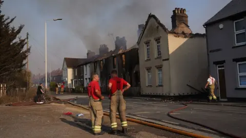 PA Media Firefighters at the scene of a blaze that destroyed a number of homes in Wennington, Essex