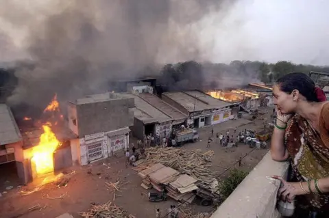 AFP This picture taken 28 February 2002 shows Ahmedabad resident Jaiwantiben watching a wood market burning after it was set ablase by Muslims that fled the Lathi bazar area in Ahmedabad.