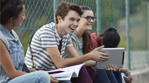 Getty/Klaus Vedfelt Friends laughing together at school, holding tablet and books