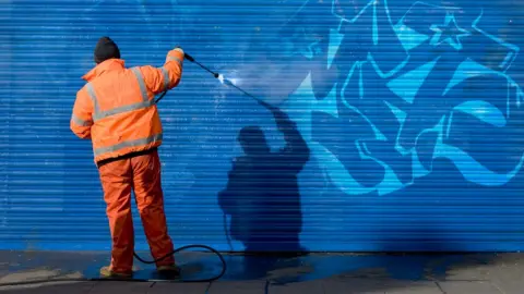Getty Images Man in hi-vis washes graffiti off garage door