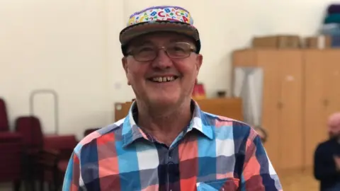 BBC Joe Hoare wearing a plaid shirt and a colourful cap