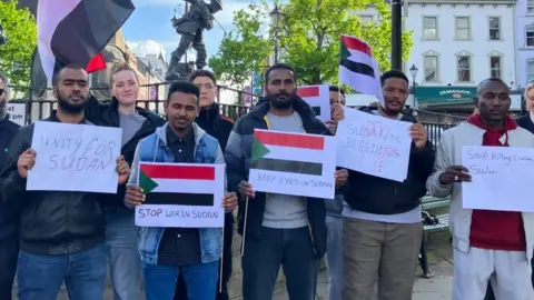 BBC Men and women hold placards and flags at a vigil for the Sudanese community in Londonderry