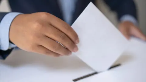 Getty Images A close up shot of a hand placing a ballot into a ballot box