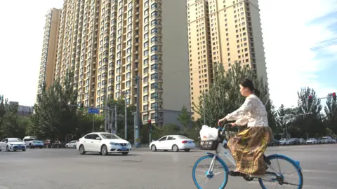 EPA A woman rides a bicycle past an Evergrande housing complex in China's capital Beijing on 28 September 2023