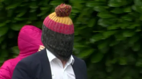 BBC Paul McAloon wears a yellow, red and black bottle hat as he walks towards court