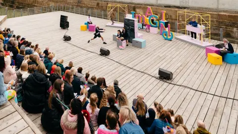 T Arran People sitting at an open air auditorium watching a play