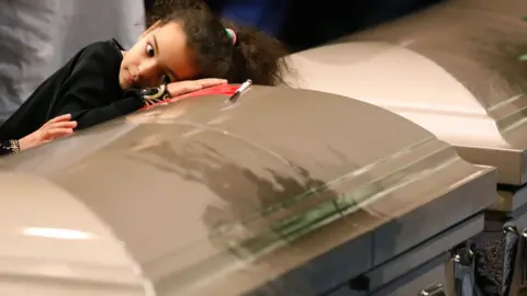 AFP A young mourner lays her head on one of the caskets during funeral services for three of the victims