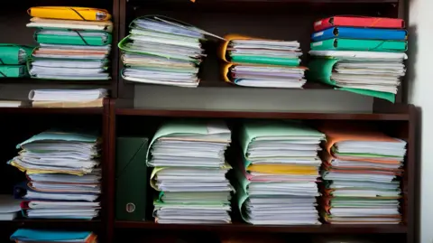 Getty Images Multiple folders in a bookcase with many pieces of paper in each one.